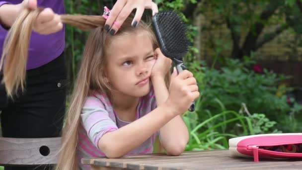 Lány unatkozik, amíg anyám zsinórt, hosszú haja, és nézi a tükörképét a tükörben — Stock videók
