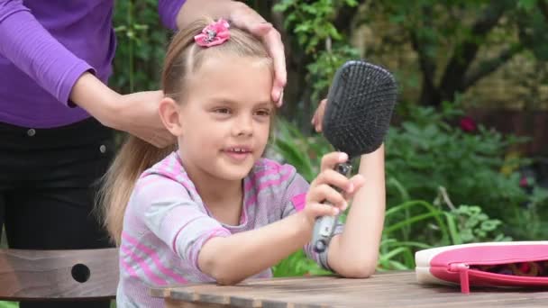 Meisje onderzoekt zichzelf in de spiegel tijdens het kammen van haar moeder — Stockvideo