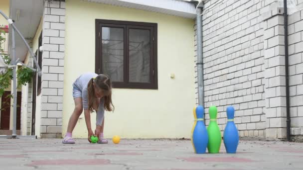 П'ятирічна дівчинка грає в дитячому боулінгу на подвір'ї — стокове відео