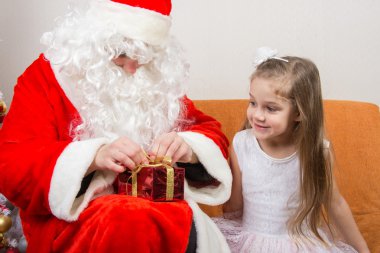 Santa Claus helps to untie the ribbon gift, little girl happily looking at him clipart