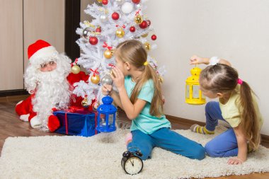 Noel Baba hediyeleri Noel ağacının altında gizli bir şekilde koymak için çalışan görmek için iki kızla el feneri