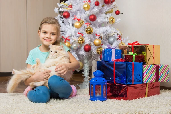 Радостная семилетняя девочка с котом, сидящим под елкой с подарками — стоковое фото