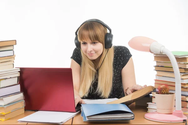 Estudiante feliz con auriculares sentados en la mesa y buscando la información que necesita en un portátil —  Fotos de Stock