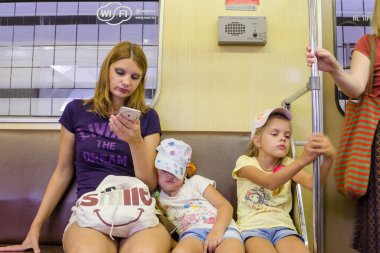 Moskova, Rusya - 10 Ağustos 2015: Moskova Metro tren durumda, annesi telefon görünüyor, küçük kızı uyurken, can sıkıntısı için korkuluk tutunmuş en büyüğü