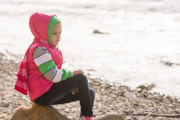 Задумчивая девушка сидит на скале на каменистом пляже моря и смотрит вдаль — стоковое фото