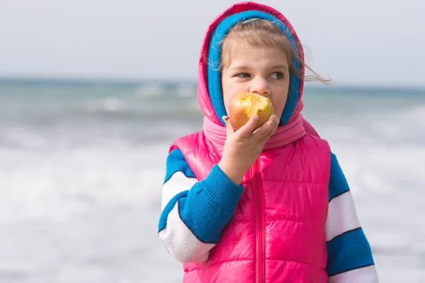 Menina de cinco anos comendo uma maçã no fundo da costa do mar — Fotografia de Stock
