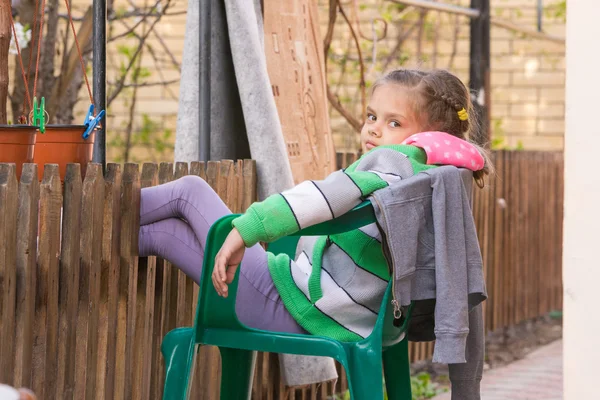 Siedem lat dziewczyna odpoczywa siedzi na krześle na podwórku i kładąc nogi na drewnianym ogrodzeniu — Zdjęcie stockowe