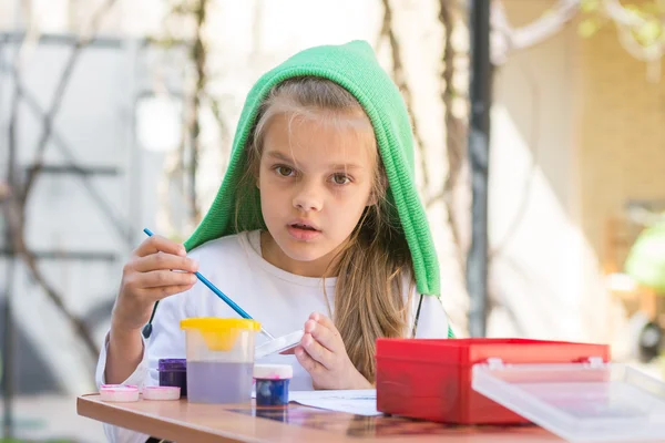 Menina desenha pinturas no quintal no dia ensolarado primavera e olhou para o quadro — Fotografia de Stock