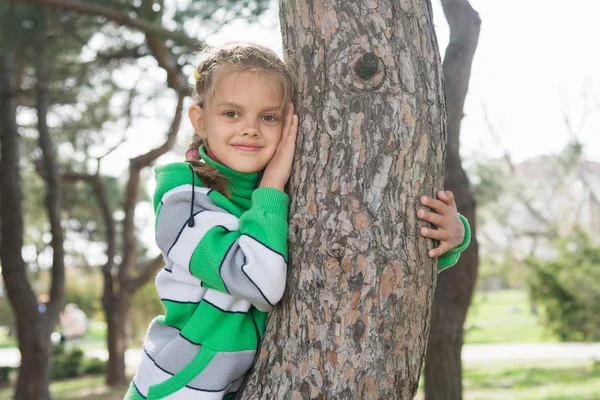 Joyful sjuårig flicka sitter på en trädstam i början av våren — Stockfoto