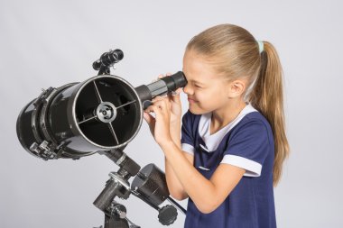 Seven-year girl squinting with interest looks in a reflector telescope clipart