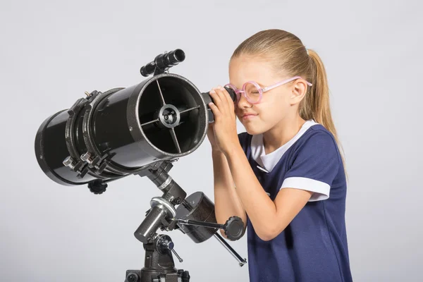 Sjuårig flicka i glasögon med intresse ser ut i en reflektor teleskop — Stockfoto