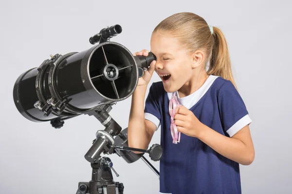 Siedem lat dziewczyna z zainteresowaniem i usta otworzyć, patrząc na teleskop reflektor i patrzy na niebo — Zdjęcie stockowe