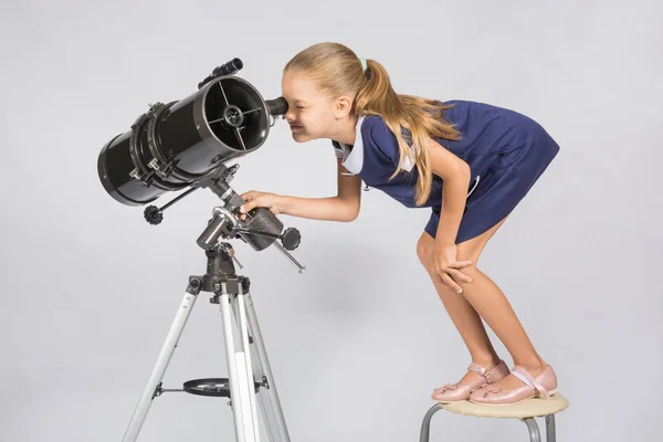 Chica de siete años de pie en una silla y se ve ridículo en el ocular del reflector del telescopio — Foto de Stock