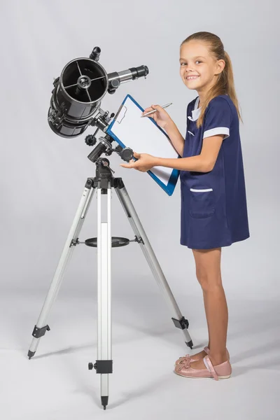 Chica feliz astrónoma se ve feliz en la imagen de pie junto al telescopio —  Fotos de Stock