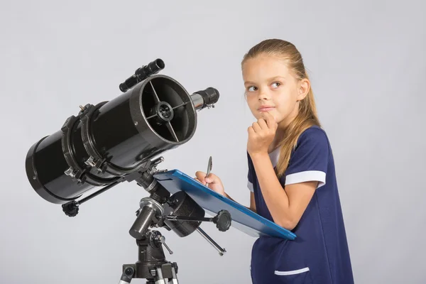 Menina de sete anos pensativa olhando para o céu, fazendo a gravação de observações no telescópio — Fotografia de Stock