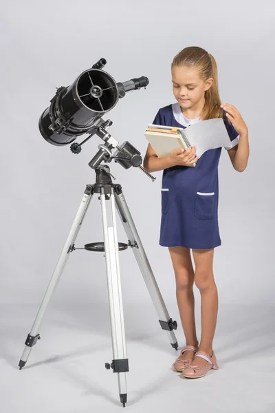 翻阅一本教科书，而站在望远镜的女生 — 图库照片