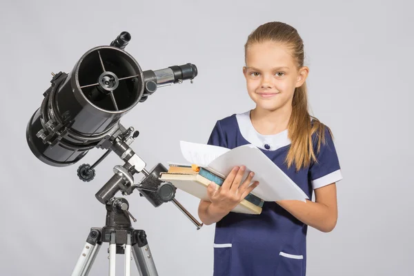 Schoolgirl astronomer leafing through books standing at the telescope — Stock Photo, Image