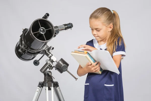 Schoolgirl astronomer leafing through books to find the right information at the stand of the telescope — Stock Photo, Image