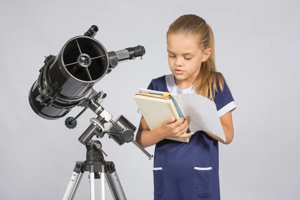 Schoolgirl reading a textbook while standing astronomer at the telescope — Stock Photo, Image