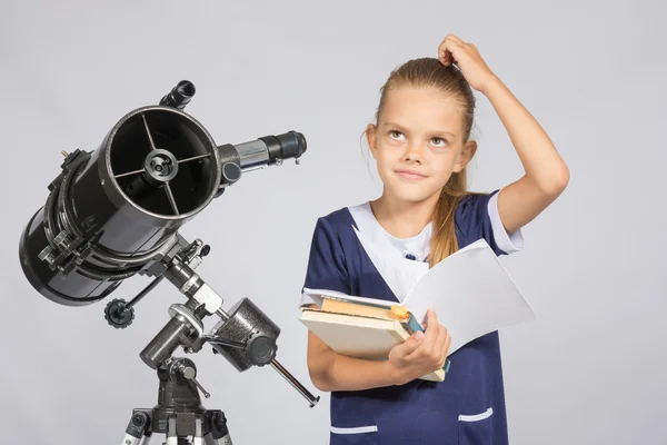 Школьница задавалась вопросом и смотрела на, читая учебник, стоя у телескопа — стоковое фото