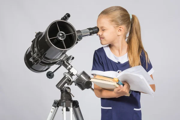 Schulmädchen blickt durch ein Teleskop, das mit Schulbüchern steht — Stockfoto