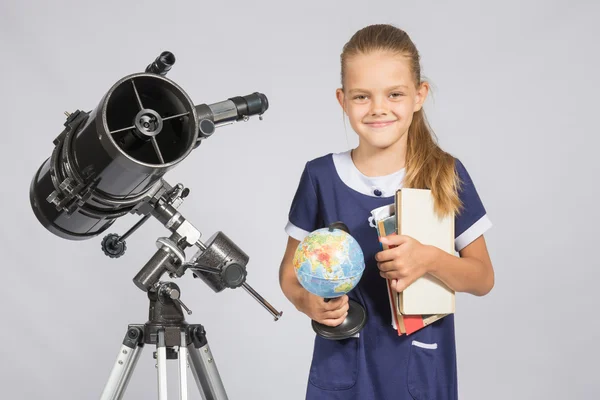 Meisje astronoom is een telescoop met een globe en boeken in de handen — Stockfoto