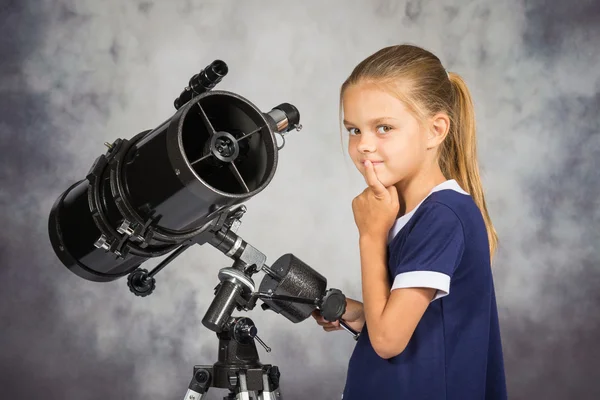 Niña de siete años cuidadosamente mira en la imagen, de pie en el telescopio — Foto de Stock