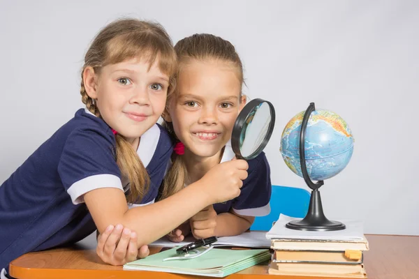 Twee schoolmeisjes kijken naar globe door een vergrootglas — Stockfoto