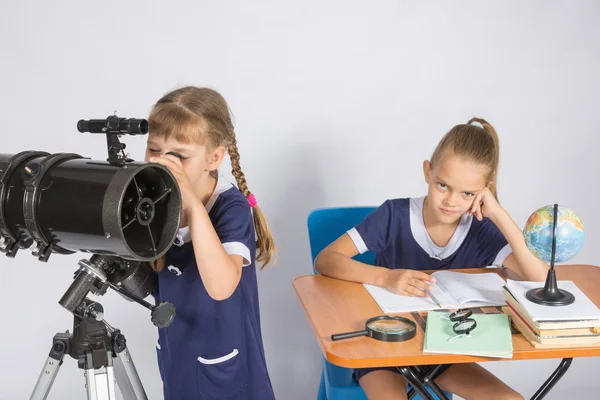 Fille astronome regarde le ciel à travers un télescope, l'autre fille est assise à la table — Photo