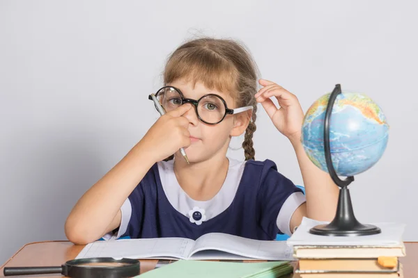 Schoolmeisje corrigeert bril tijdens de vergadering op een bureau in de klas Geografie — Stockfoto