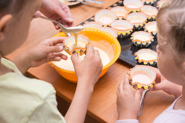Two girls helped mom to pour batter into the molds for cupcakes