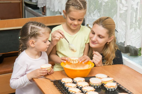 The elder daughter pours batter for cakes in tins, under the care of my mother and younger sister — Stock Photo, Image