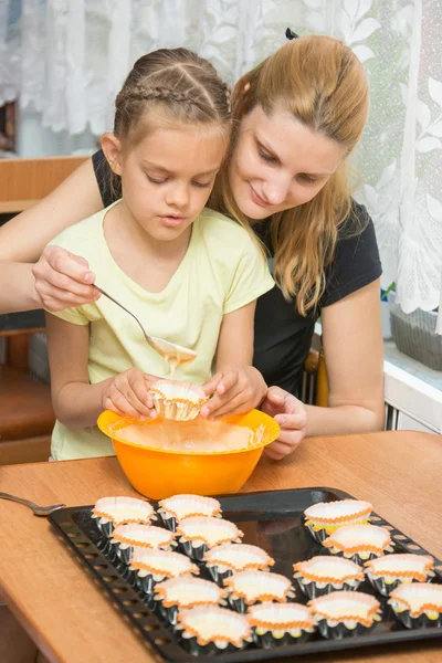 Мама помогает дочери налить тесто в плесень для кексов — стоковое фото