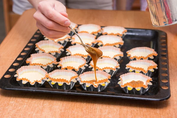 Gekochte Kondensmilch, die rohen Cupcakes auf einem Backblech liegendes Werkstück hinzugefügt wird — Stockfoto