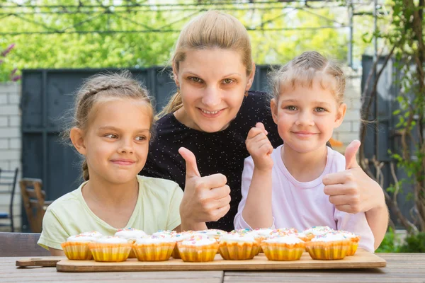 Mor och två döttrar visar en tummen upp, och klä påsk cupcakes — Stockfoto