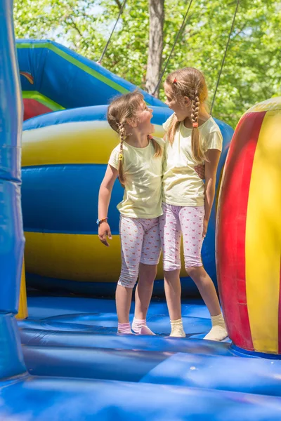 Dwie dziewczyny grymasy szczęśliwie patrząc na siebie skacząc na trampoliny nadmuchiwane — Zdjęcie stockowe