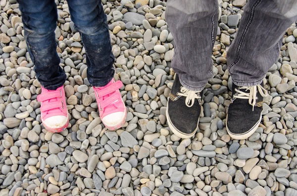 Dois pares de pés em tênis, adultos e crianças, estão no calhau — Fotografia de Stock