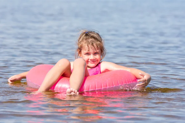 Пятилетняя девочка плавает в реке, сидит на коленях, плавая и счастливо смотрит в раму — стоковое фото
