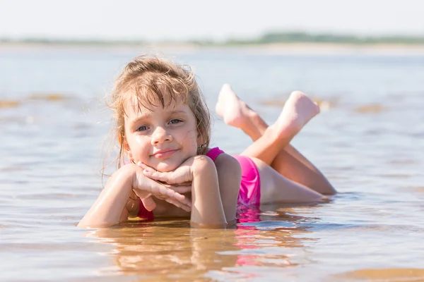 Пятилетняя девочка лежит в воде на мелководье реки — стоковое фото