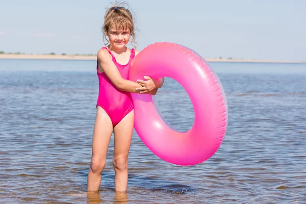 Пятилетняя девочка в розовом купальнике стоит с плавающими кругами в реке — стоковое фото