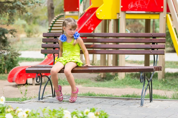 Boos meisje beetje haar lip zittend op de Bank op de achtergrond van de speeltuin — Stockfoto