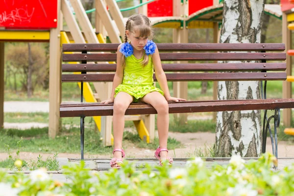 Jeune fille pleurant assise sur le banc sur le fond de l'aire de jeux — Photo