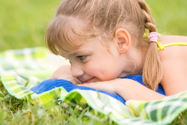 Chica de cinco años se encuentra en un prado verde y tocar mirando la hierba —  Fotos de Stock