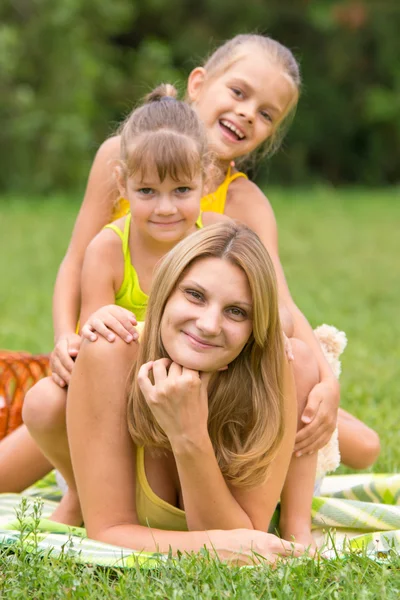 Deux filles sont assises sur la jeune mère, qui est allongée sur l'herbe verte — Photo