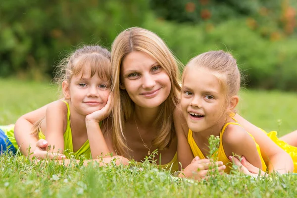 Madre y dos hijas yacen sobre la hierba verde, y miran en el marco —  Fotos de Stock