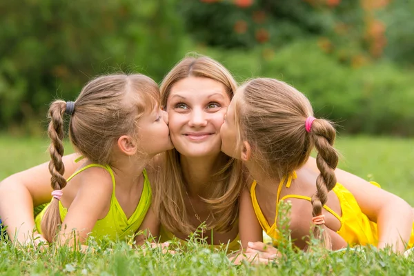 Dos hijas besándose madre acostada en el césped en un picnic, madre miró hacia arriba diversión — Foto de Stock