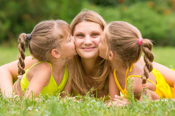 Duas filhas beijando a mãe deitada na grama em um piquenique — Fotografia de Stock