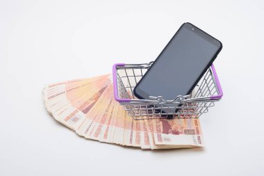 Beş bininci banknotun arka planında üzerinde cep telefonu olan bir market sepeti var.
