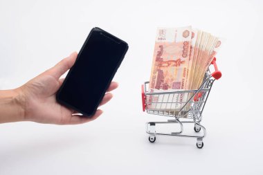 Bir el akıllı telefonu tutar, market arabasının yanında beş bin dolarlık banknotlar yatar.