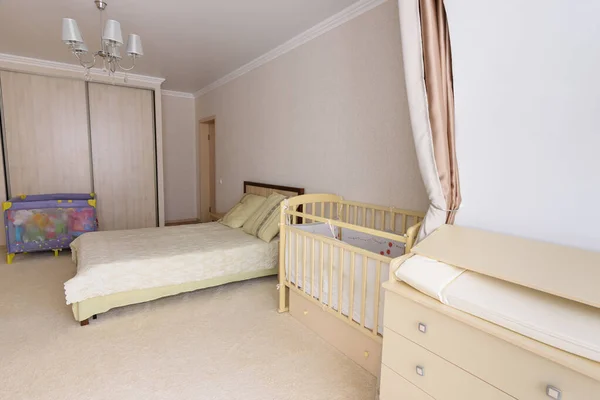 Sleeping room converted for a newborn baby, there is a changing table, a cot and a playpen